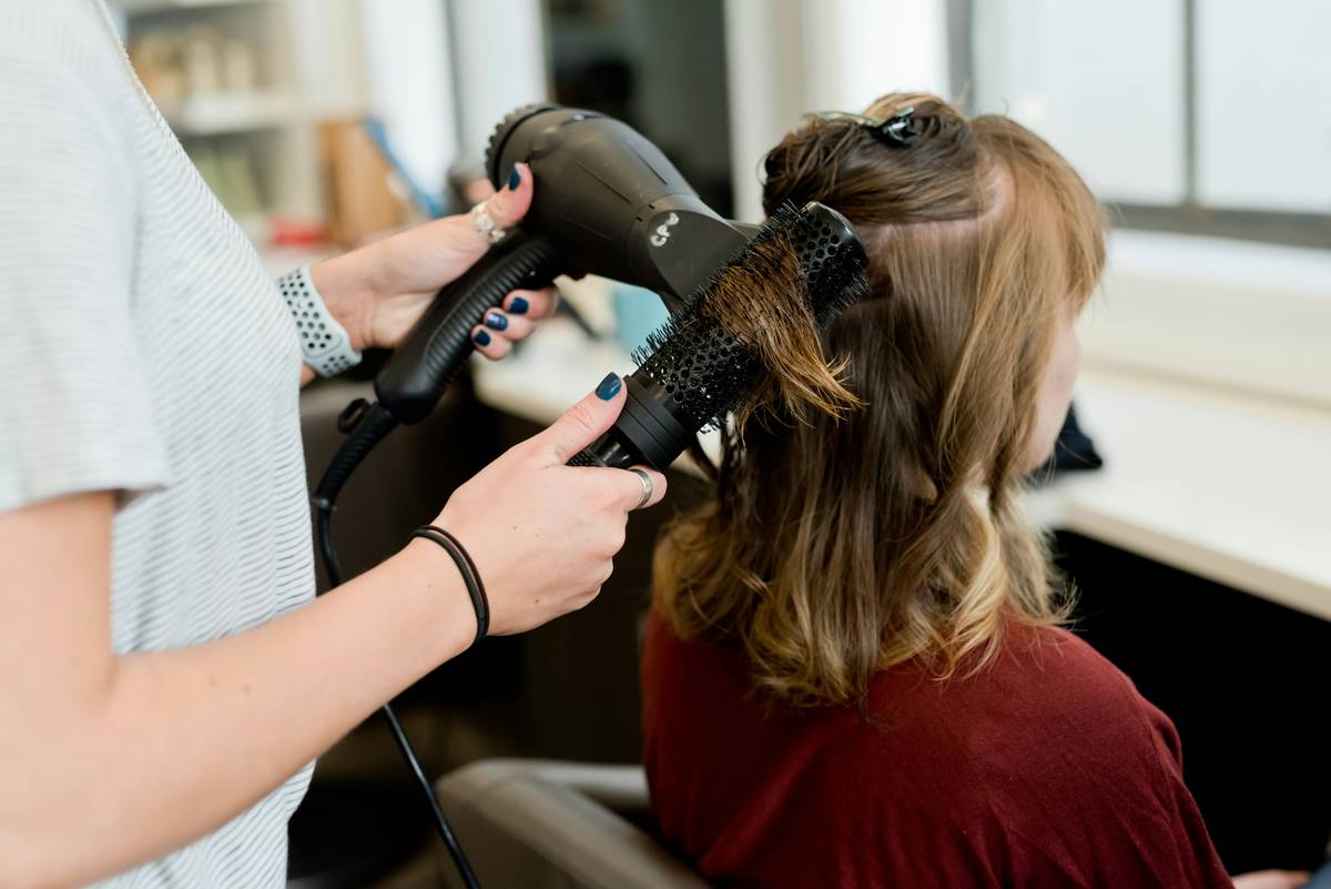 Woman applying hair recovery spray to damp mid-lengths in bathroom mirror