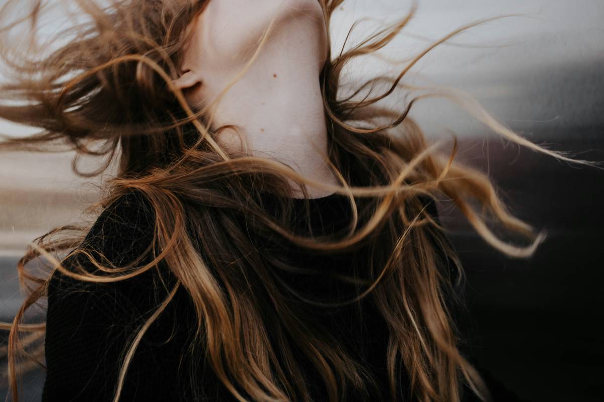 Woman spritzing hair fortifying spray on damp hair near roots for volume and strength